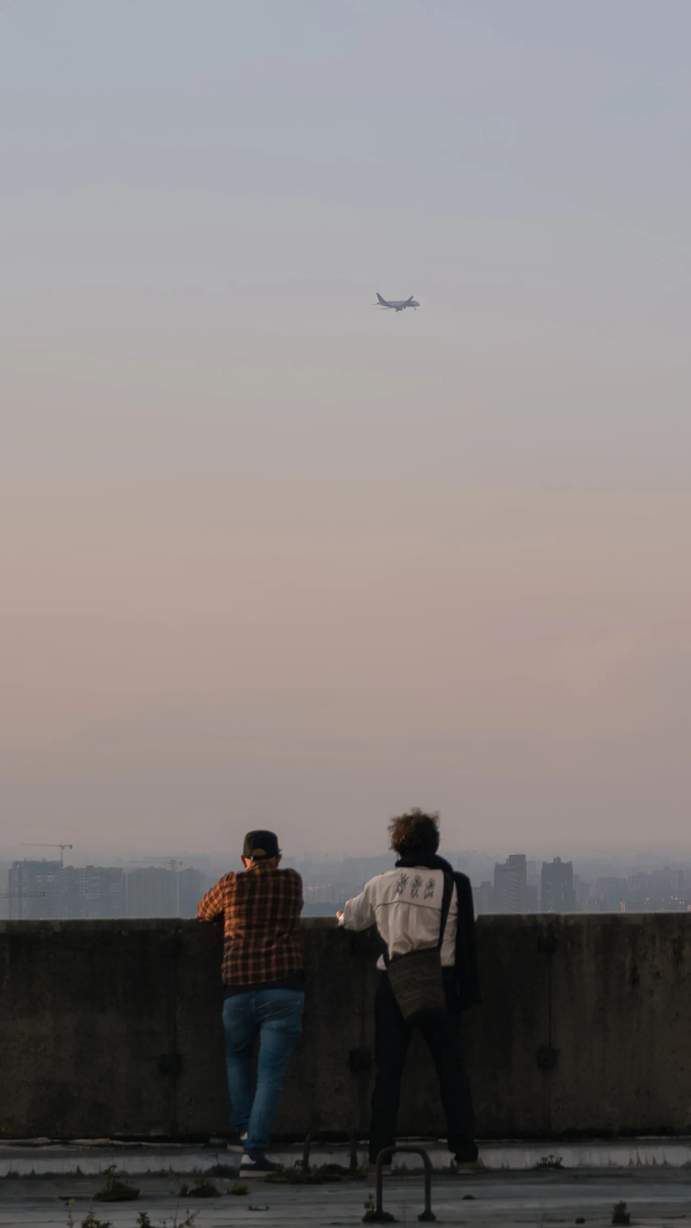 Dos personas asomadas al borde de una azotea sobre Bogotá al atardecer, con un avión en el cielo