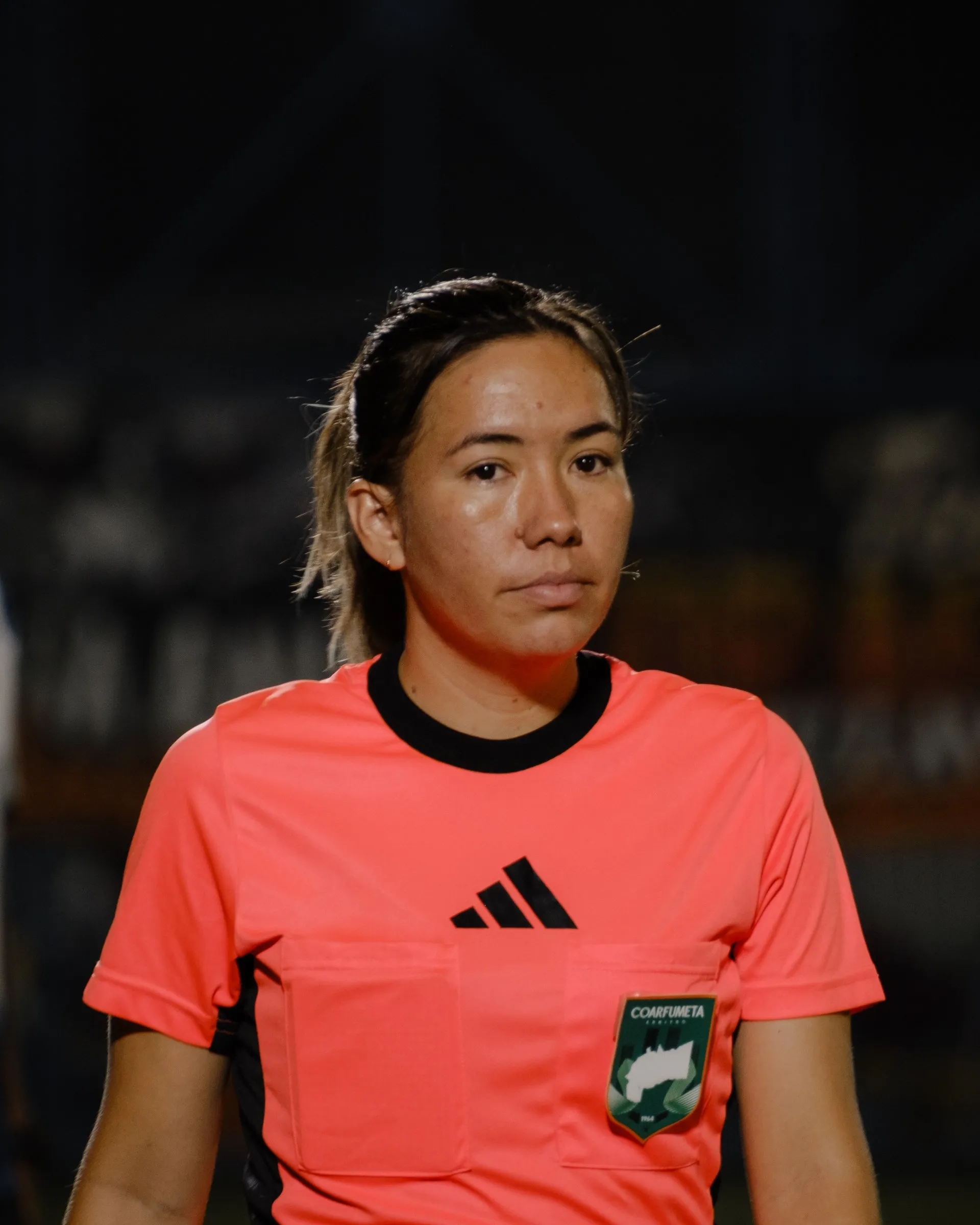 Árbitra de camiseta naranja bajo las luces del estadio