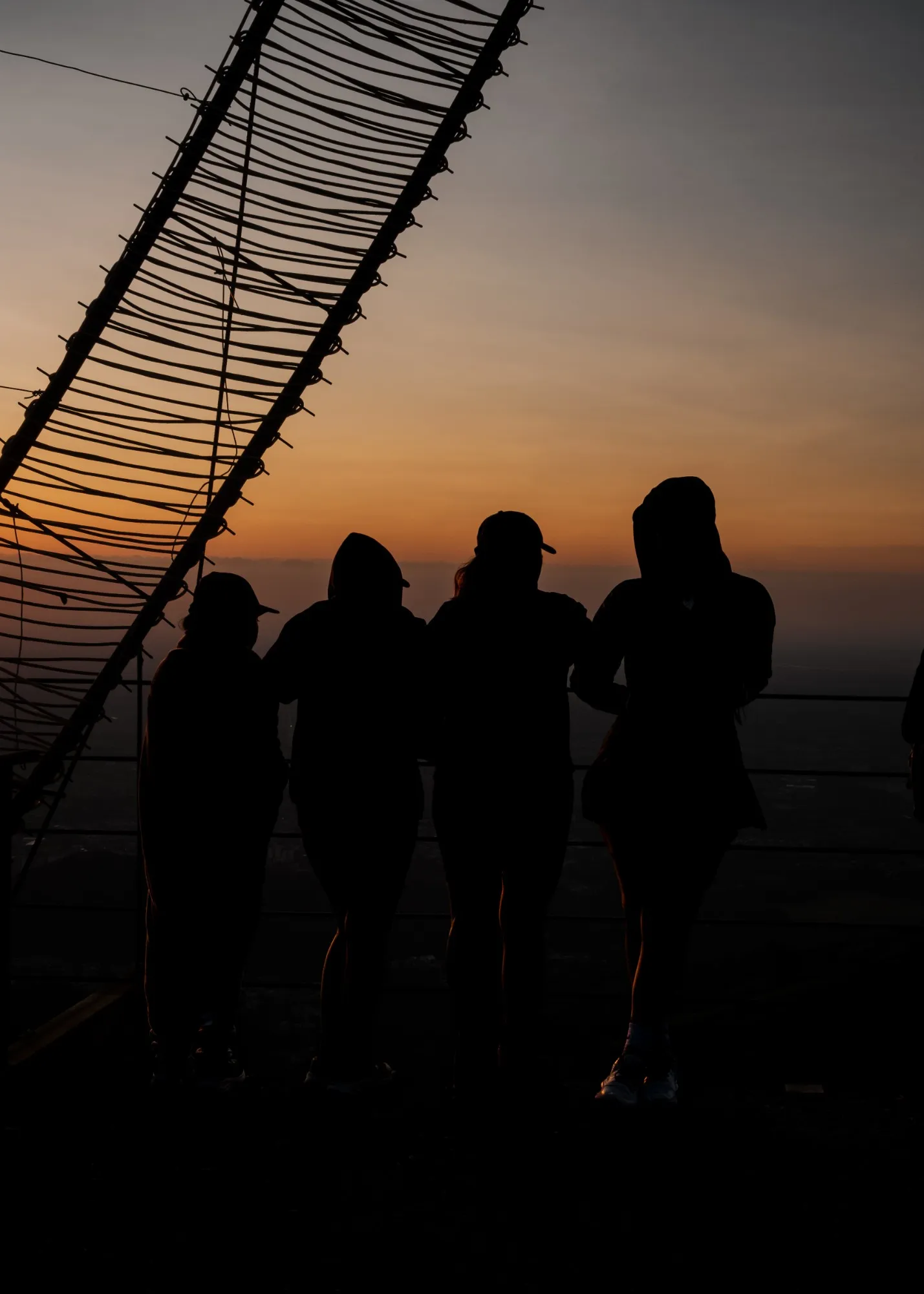 Cuatro senderistas a contraluz en la baranda de un mirador, frente al amanecer